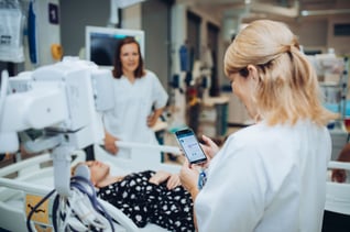 Mobil - sykepleier med pasient i bakgrunnen-1