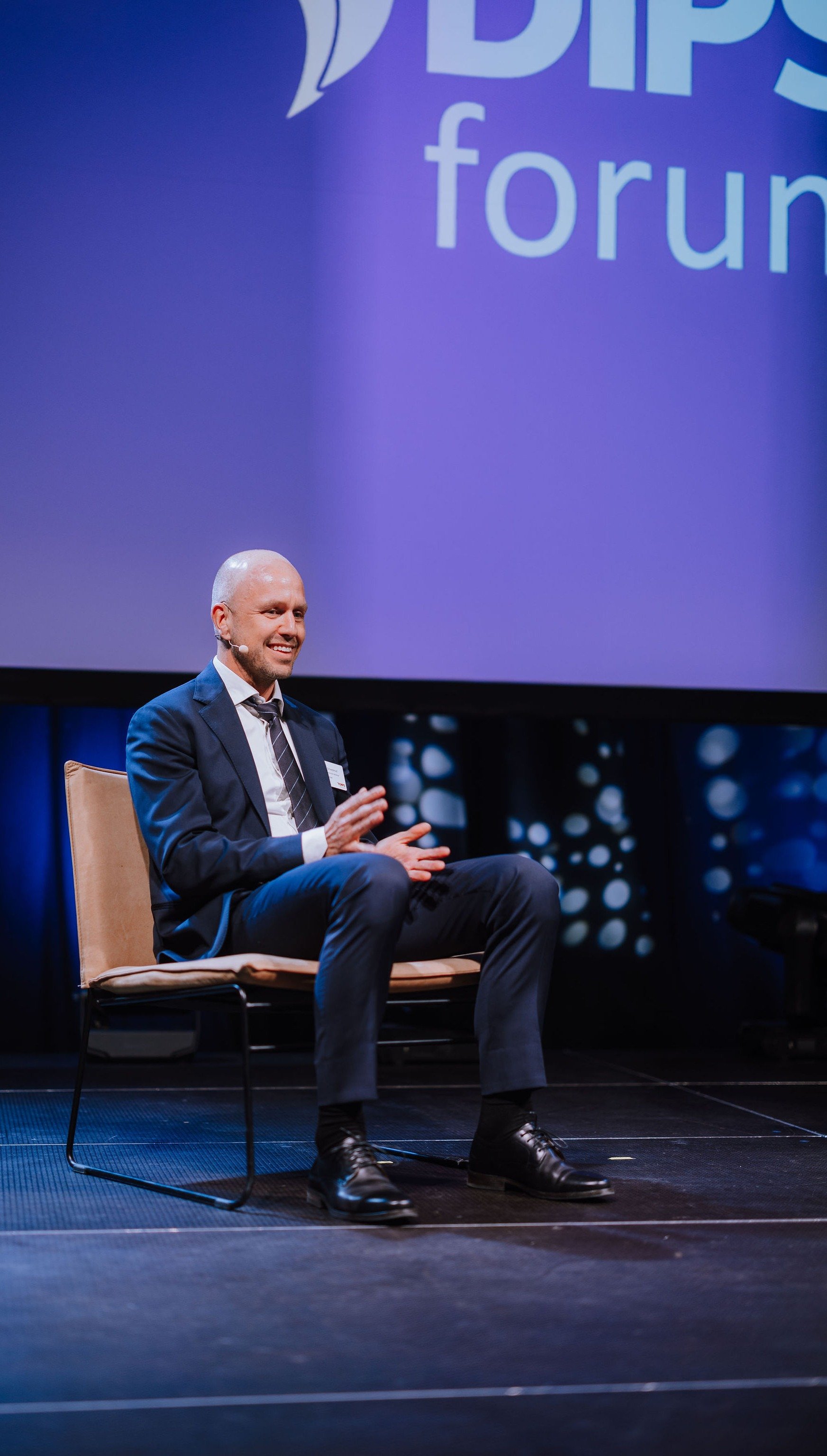 Mann som smiler i en stol på scenen under en konferanse