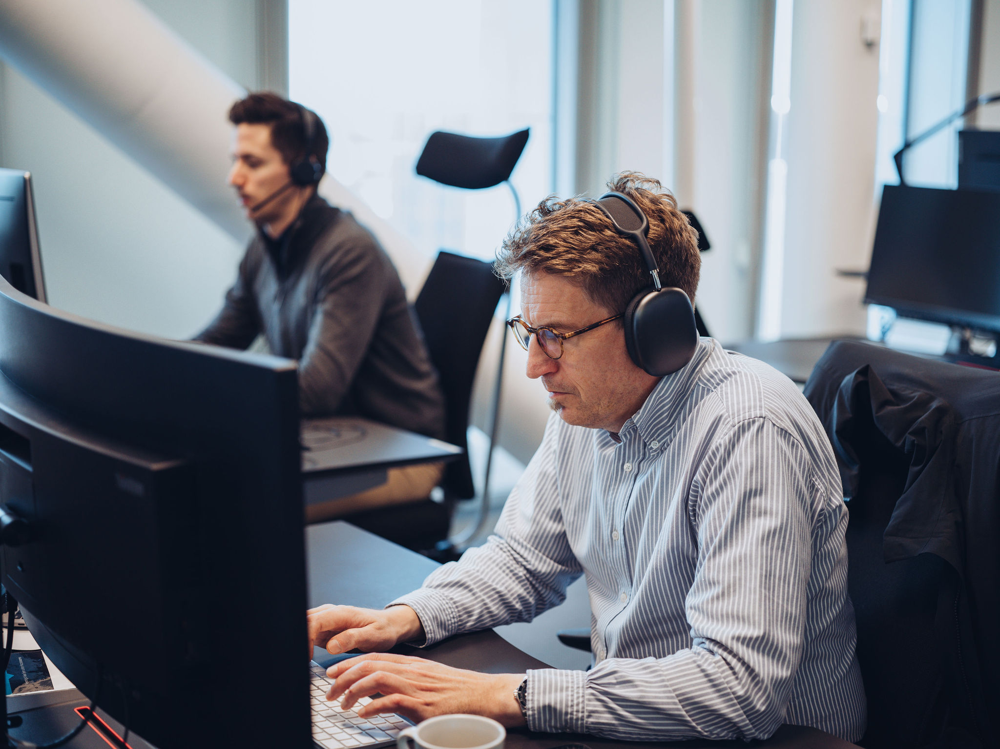 Mann med headset jobber på PC med person i bakgrunnen