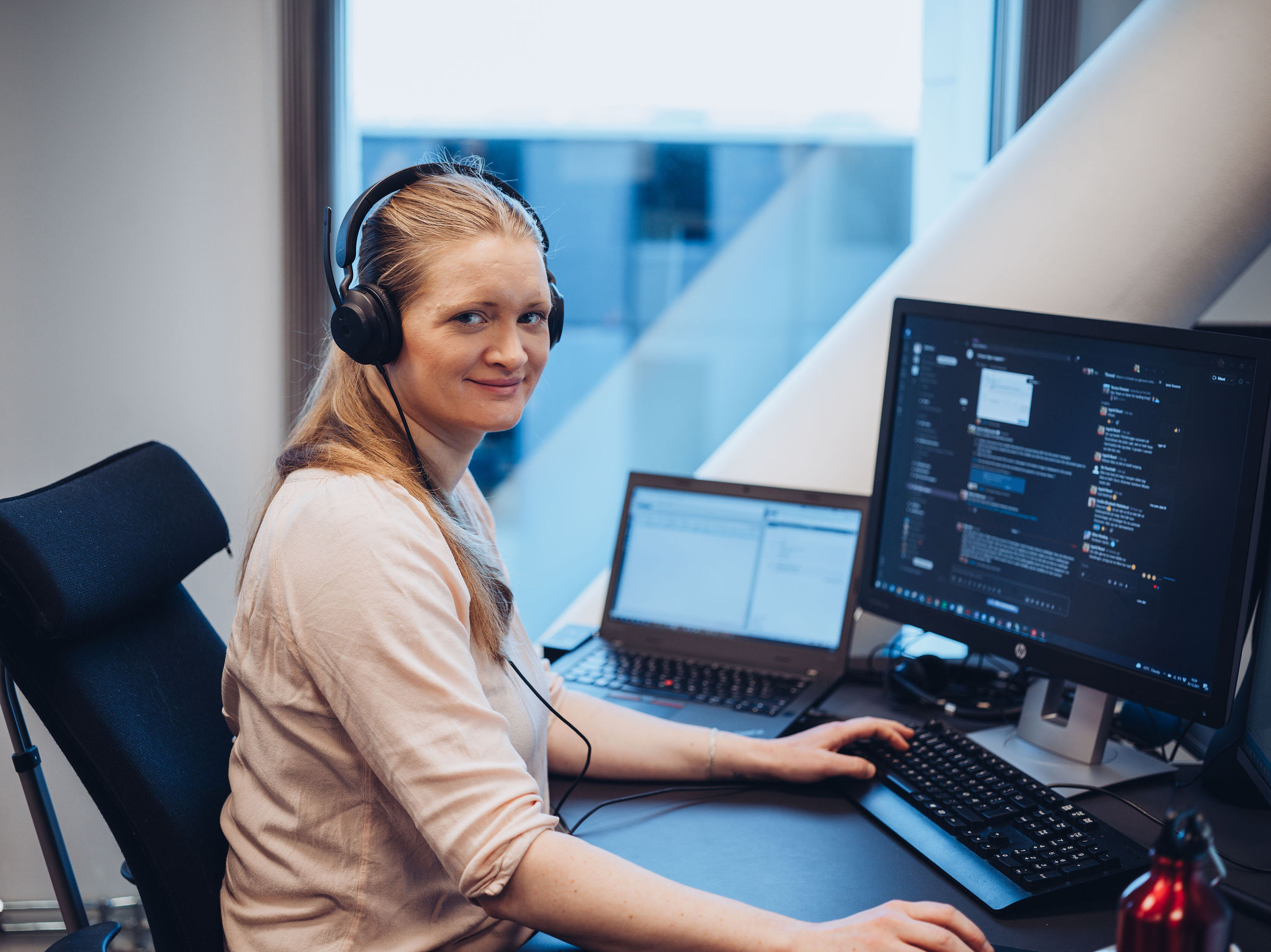 Smilende dame med headset jobber på PC