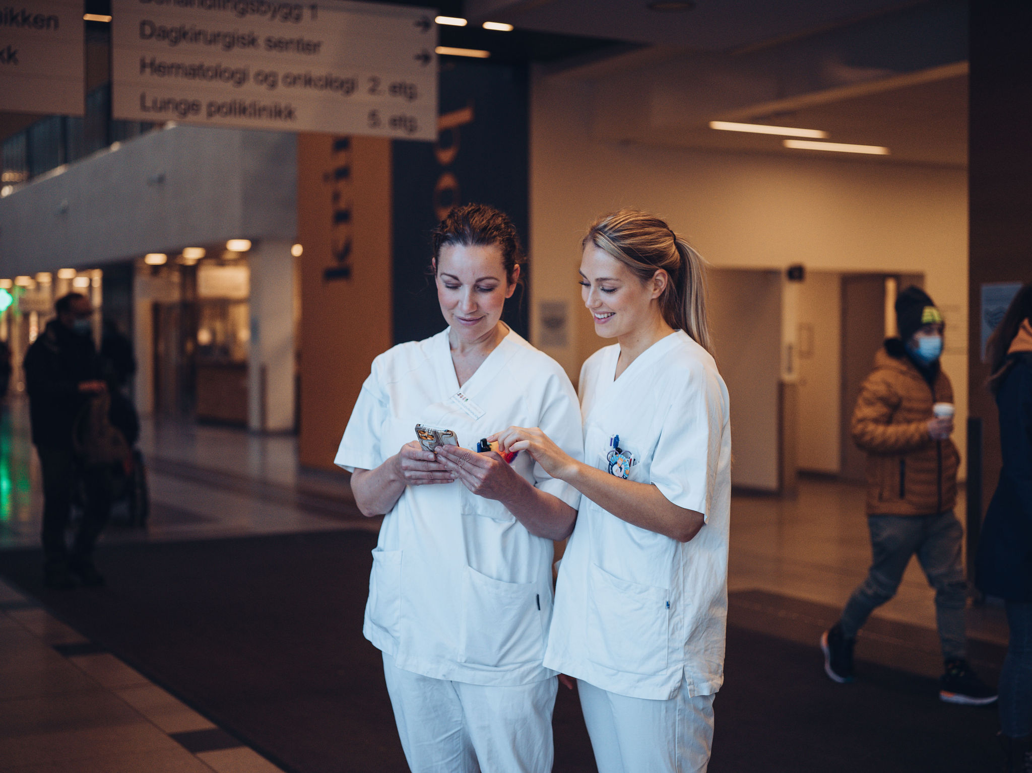 To sykepleiere ser på mobilen i alleen på Ahus 2