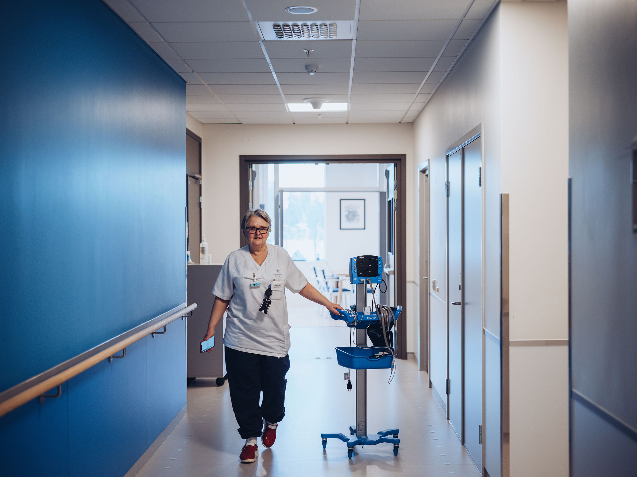 Sykepleier kommer gående med medisinsk apparat og mobil i hånden